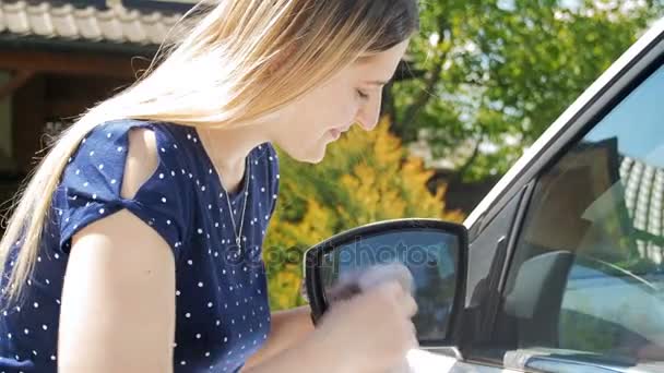 4k відео молодої усміхненої жінки, що чистить автомобіль збоку дзеркало з тканиною — стокове відео