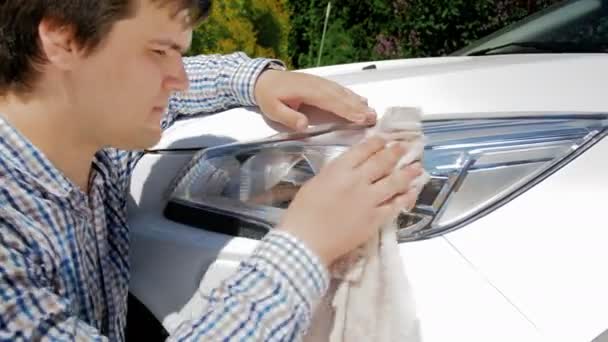 4k кадров, где молодой человек моет фары машины тканью на заднем дворе — стоковое видео