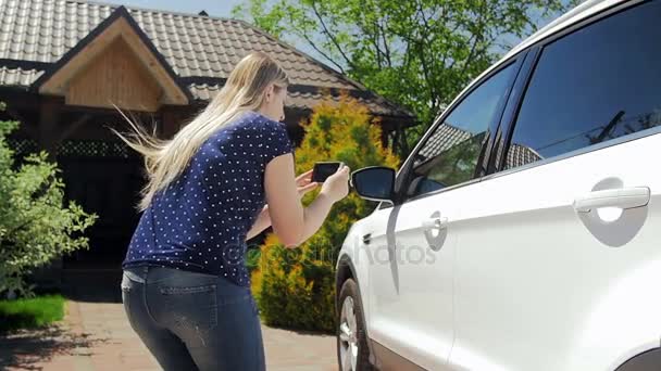 Slow motion bilder av unga kvinnliga förare att göra bilder på smartphone av hennes bil för sälja — Stockvideo
