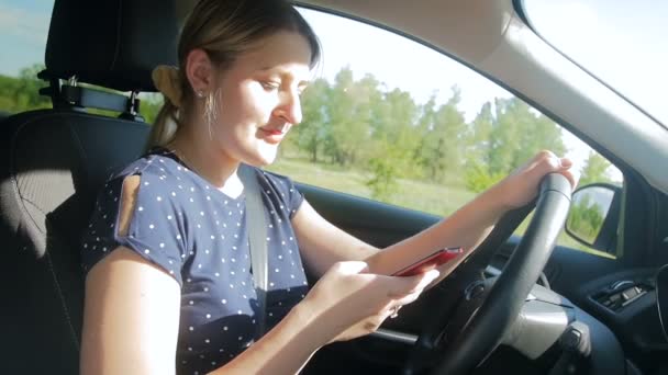 Уповільнення руху молодої жінки-водія за допомогою смартфона під час руху автомобіля по дорозі — стокове відео
