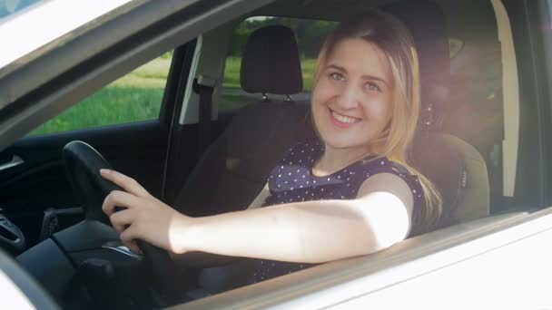 Retrato de câmera lenta de bela mulher sorridente sentada no assento do motorista de carro e olhando através da janela lateral — Vídeo de Stock