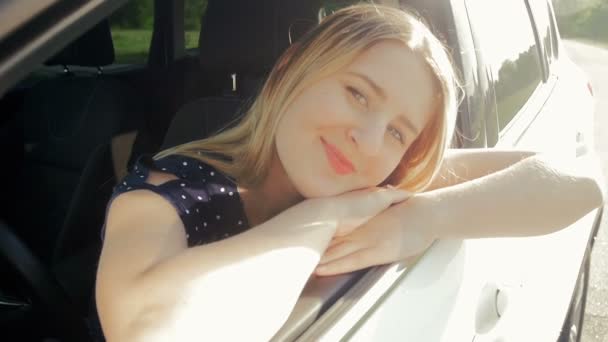 Slow-motion video van jonge lachende vrouw zit op de plaats van de bestuurder van de auto en kijken naar camera — Stockvideo