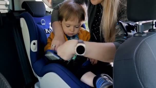 4 k video van jonge glimlachend aanpassen riemen van de moeder op haar childs veiligheid autostoel — Stockvideo