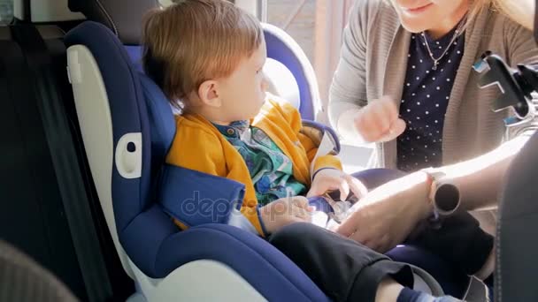 4k 年轻母亲松开腰带的镜头, 并带她的儿子从孩子安全汽车座椅 — 图库视频影像