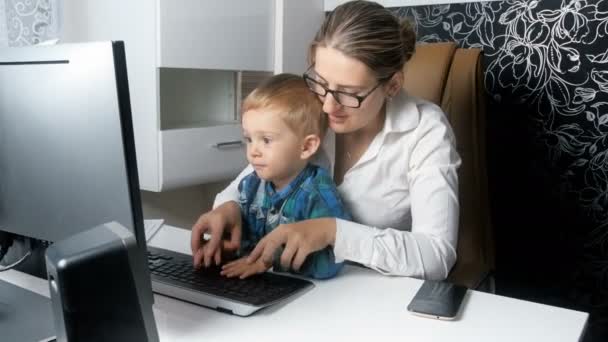 4k metraje de hermosa mujer de negocios elegante que trabaja en la computadora con su adorable hijo pequeño en la oficina — Vídeo de stock