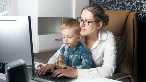 4k vídeo of young businesswoman working in office while her cute little toddler son sitting on her lap and eating — Vídeo de Stock