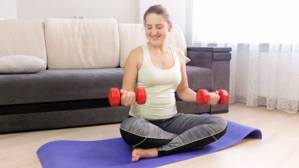 Imágenes de 4k de una hermosa joven haciendo ejercicio con pesas en una colchoneta de fitness en casa — Vídeo de stock