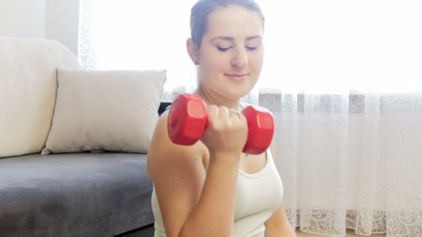 4k крупным планом кадры, где молодая улыбающаяся женщина тренируется и укрепляет мышцы рук гантелями — стоковое видео