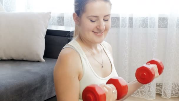 4k metraje de hermosa mujer joven levantando dos dumbbels rojos en casa — Vídeo de stock