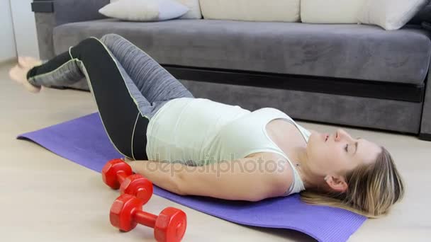 4 k video genç güzel kadın fitness mat oturma odasında egzersiz yaparken bacaklar kaldırma — Stok video