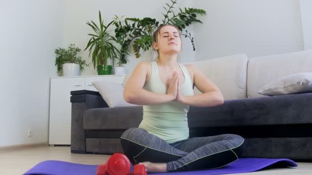 Долли 4k кадры молодой женщины, сидящей в позе лотос-йоги на фитнес-коврик дома — стоковое видео