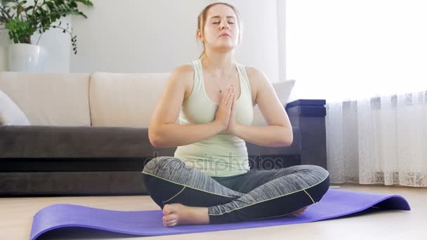 Mooie jonge vrouw mediteren en het beoefenen van yoga op fitness mat te plaatsen bij de woonkamer — Stockvideo