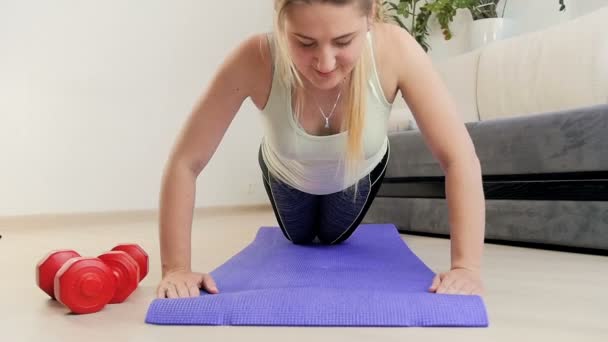 Slow motion beelden van mooie jonge vrouw doet push ups op fitness mat thuis — Stockvideo