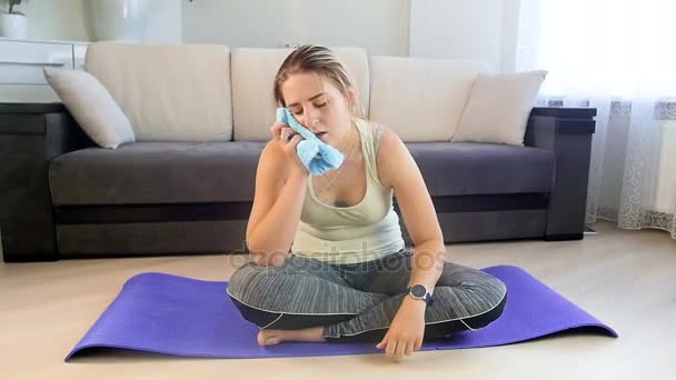 Zeitlupenaufnahmen einer erschöpften, verschwitzten Frau, die nach dem Training zu Hause auf einer Fitnessmatte sitzt — Stockvideo