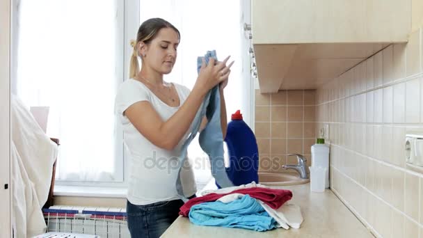 4k видео красивой молодой женщины складывая и неся чистую одежду из прачечной — стоковое видео