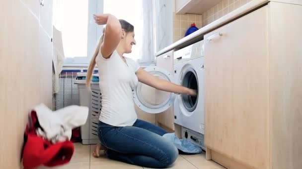 Slow motion video of happy laughing woman taking clothes out of washing machine and throwing in air — Stock Video