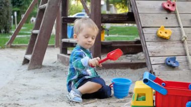 Kaplama ve kırmızı plastik kürekle kum kum kazma gülümseyen yakışıklı Slow motion video