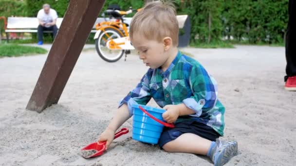 おもちゃで遊ぶかわいい幼児男の子のスロー モーション ビデオ シャベルし、遊び場でサンド ボックスでバケット — ストック動画