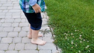 Asfalt yol üzerinde duran ve Park'ta taze yeşil çimenlerin üzerinde adım için çalışıyor yalınayak küçük çocuk ağır çekim görüntüleri