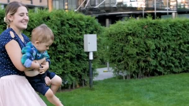 Vidéo au ralenti de la jeune mère joyeuse tenant son fils tout-petit et filant sur l'herbe au parc 