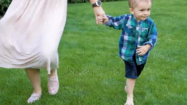 Video al rallentatore di adorabile bambino scalzo che tiene per mano le madri e cammina sull'erba al parco — Video Stock