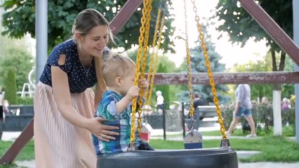 Slow motion footage of adorable 2 years old toddler boy riding on swing on playground at park — Stock Video