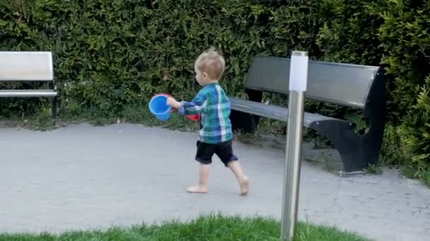 Imágenes en cámara lenta del lindo niño descalzo corriendo en el patio de recreo con pala de juguete y cubo — Vídeo de stock