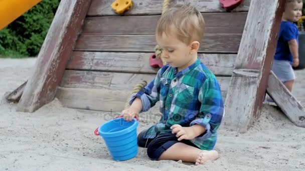 Vídeo em câmera lenta de menino bonito da criança cavando buraco na caixa de areia no playground no parque — Vídeo de Stock