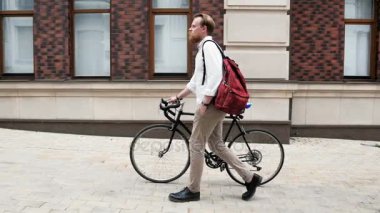 Kırmızı çantalı bicyclec ile sokakta yürüyen genç sakallı adam Slow motion video