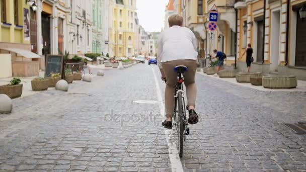 Imágenes de la vista trasera de un joven elegante montando en bicicleta en el viejo camino pavimentado — Vídeos de Stock