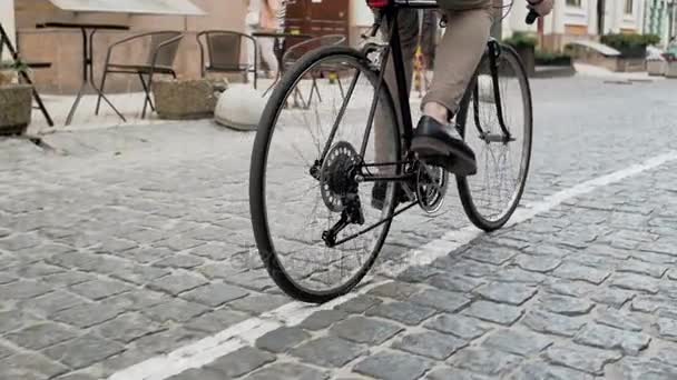 Низкий угол съемки стильного молодого человека, поворачивающего педали велосипеда во время поездки на работу — стоковое видео