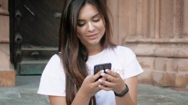 4 k görüntüleri eski taş merdivenlerde oturan ve cep telefonuyla güzel gülen esmer kadın