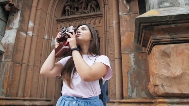 Vidéo au ralenti d'une jeune femme souriante faisant des photos de la vieille ville sur une caméra de film manuelle — Video