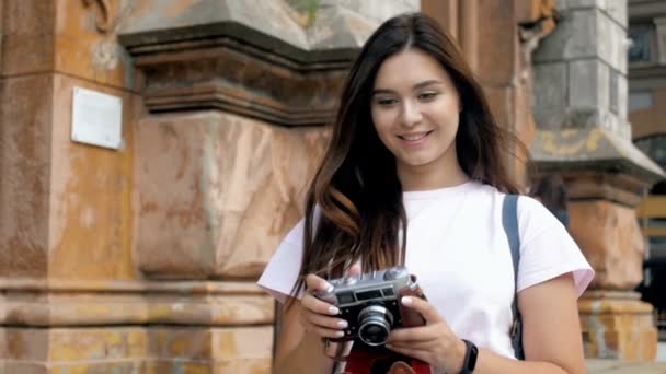 Filmagem em câmera lenta de uma jovem sorridente andando na rua e fazendo fotografias com câmera vintage — Vídeo de Stock