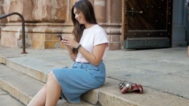 Sokakta oturan ve smartphone kullanarak güzel turist kız ağır çekim görüntüleri