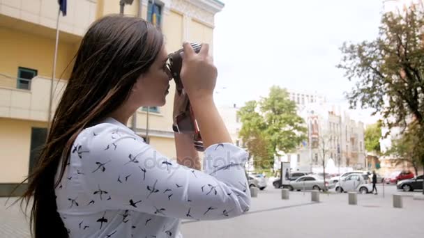Closeup slow motion footage of beautiful brunette girl with long hair using vintage manual camera on street — Stock Video