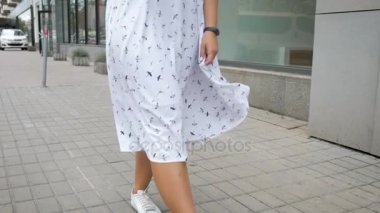 Güzel neşeli kız elbise ve spor ayakkabı sokakta yürürken Slow motion video