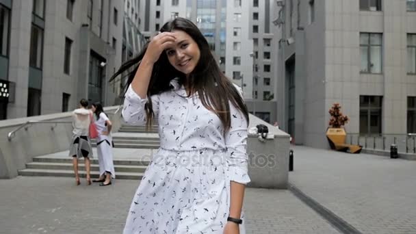 Filmagem em câmera lenta de uma bela mulher sorridente com longos cabelos escuros andando na rua moderna — Vídeo de Stock