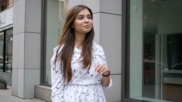 Slow motion footage of beautiful young woman walking on street and playing with her long hair — Stock Video