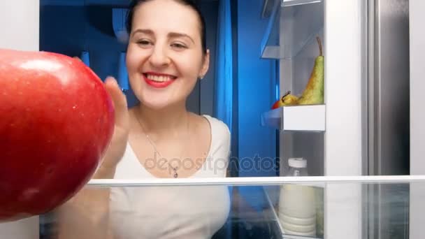 4k vídeo de bela mulher sorridente tomando maçã vermelha da geladeira — Vídeo de Stock