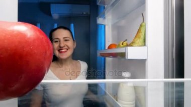 buzdolabı ve ısırıkları kırmızı sulu elma genç gülümseyen kadın 4 k görüntüleri açar