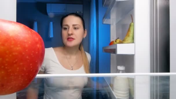 4k кадри красивої молодої жінки, яка вибирає щось поїсти в холодильнику вночі — стокове відео