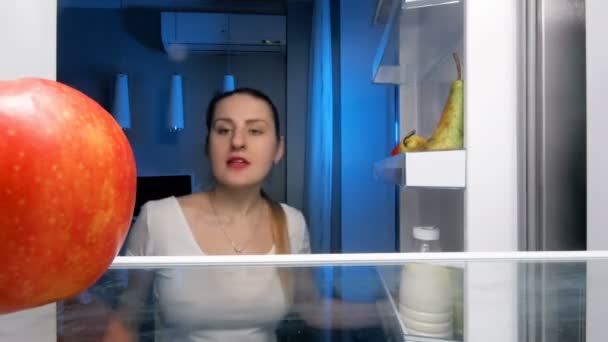 4 k footage uśmiechający się młoda kobieta, gryzienie Czerwone jabłko na kuchni w nocy — Wideo stockowe