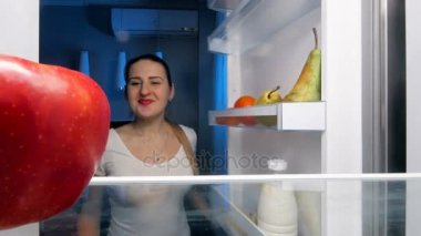 Buzdolabında seyir ve Kırmızı elma yiyen genç aç kadın 4 k görüntüleri