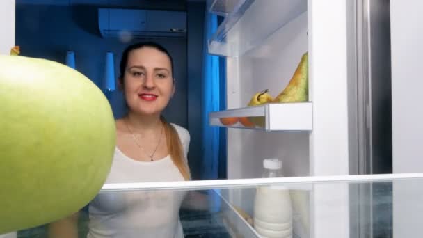 4 k felvétel, fiatal nő megnyitása hűtőszekrény és harap zöld alma — Stock videók
