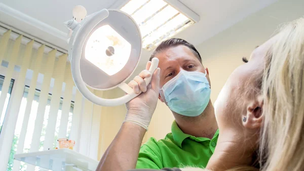 Close-up beeld van jonge mannelijke tandarts lamp voor inspectie patiënt aanpassen — Stockfoto