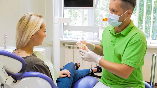 Ung kvinna sitter i tandläkare stol och diskutera sätt tänder behandling — Stockfoto