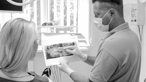 Black and white image of dentist showing x-ray image to his woman patient — Stock Photo, Image