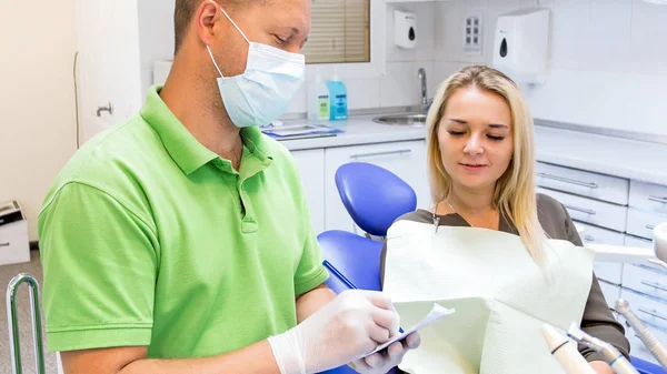 Retrato da jovem mulher sentada na cadeira do dentista enquanto o médico escreve prescrição — Fotografia de Stock