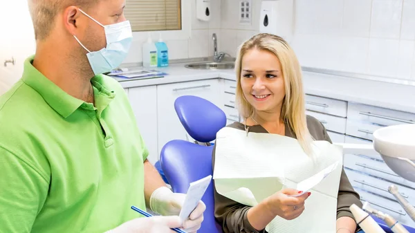 Dentista masculino dando receita para bela jovem sentada na cadeira do dentista — Fotografia de Stock